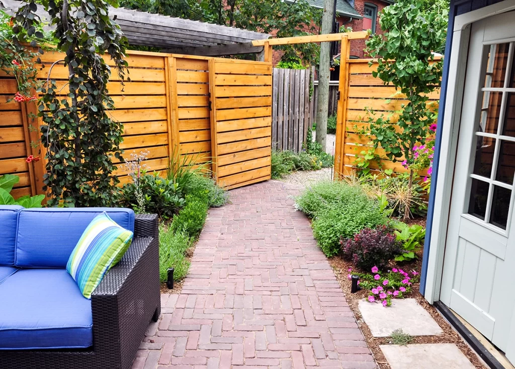 Pathway through backyard garden with wood fence and outdoor couch