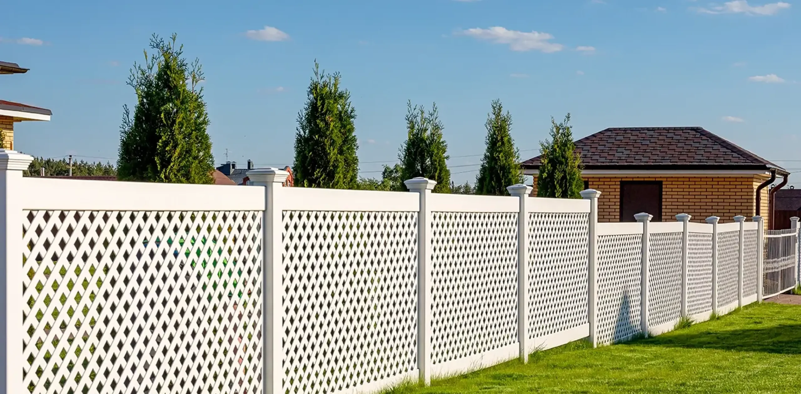 A white vinyl lattice fence in a grassy yard
