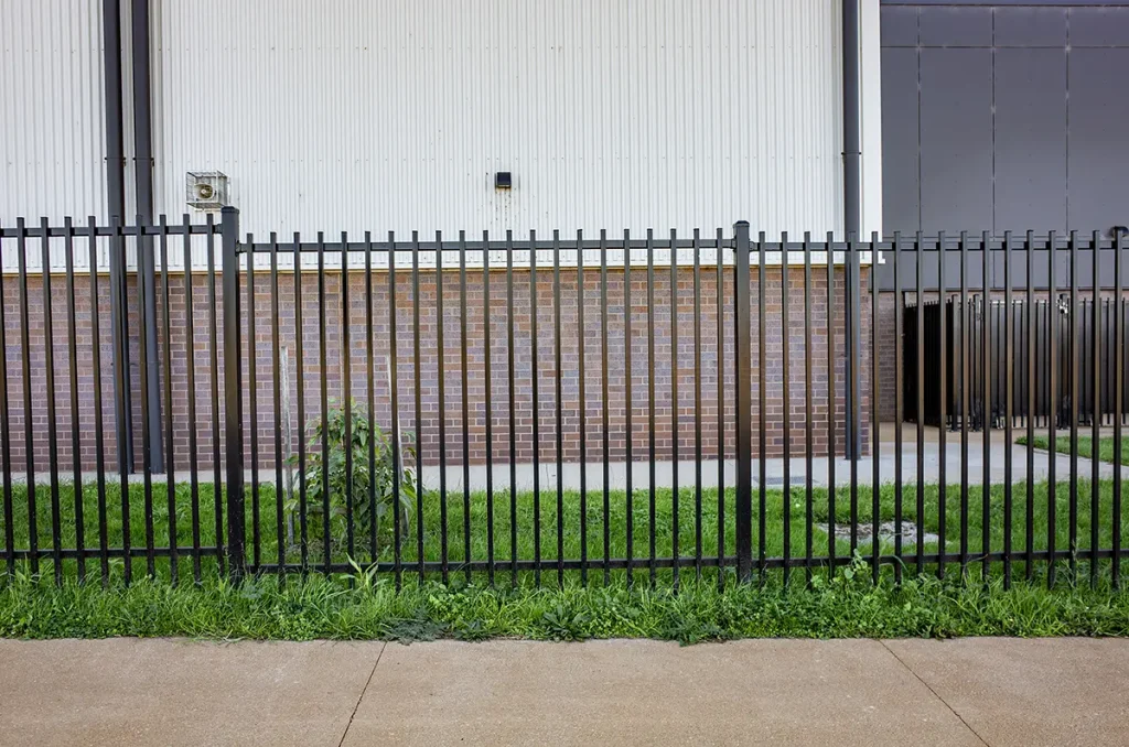 A black metal security fence installed along the exterior of a modern commercial or industrial building.